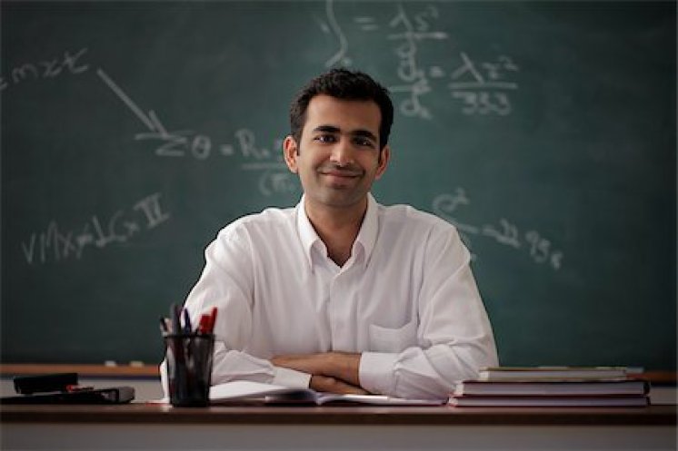849-03901398 © Asia Images / Masterfile Model Release: Yes Property Release: Yes Young man sitting at his desk smiling with chalk board behind